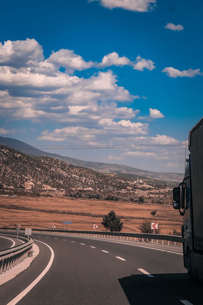 services-09 A large truck travels on a winding countryside highway beneath a clear blue sky with scattered clouds.