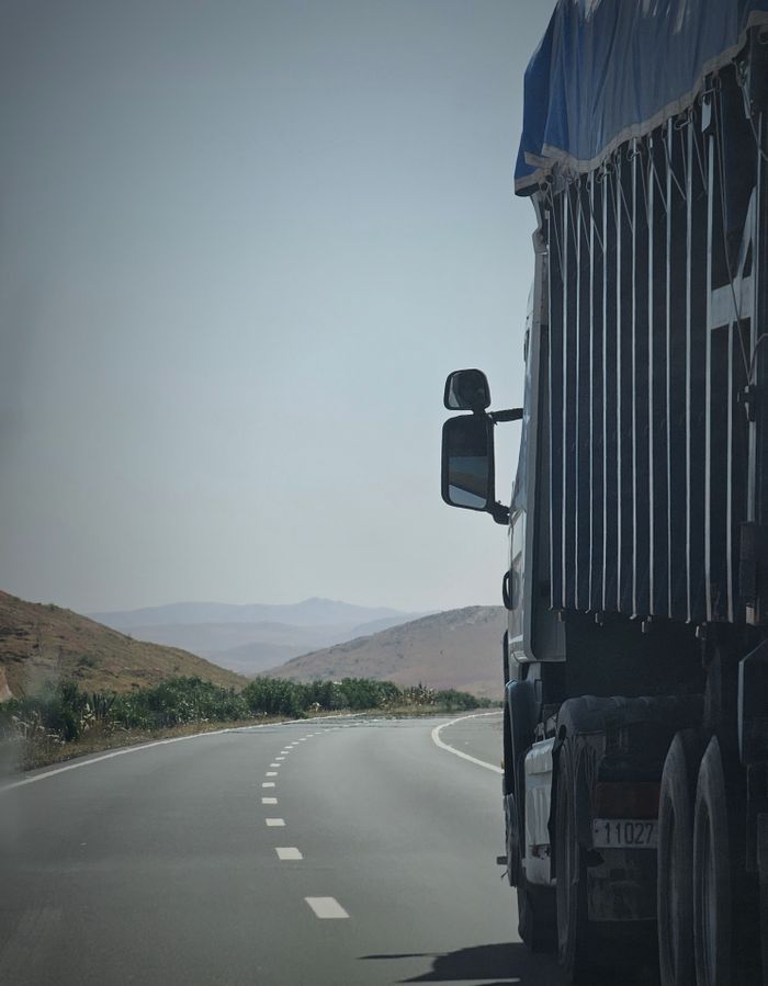 Truck on a winding highway in Douar Ouled El Mesnaoui, Morocco, set in a rocky landscape.