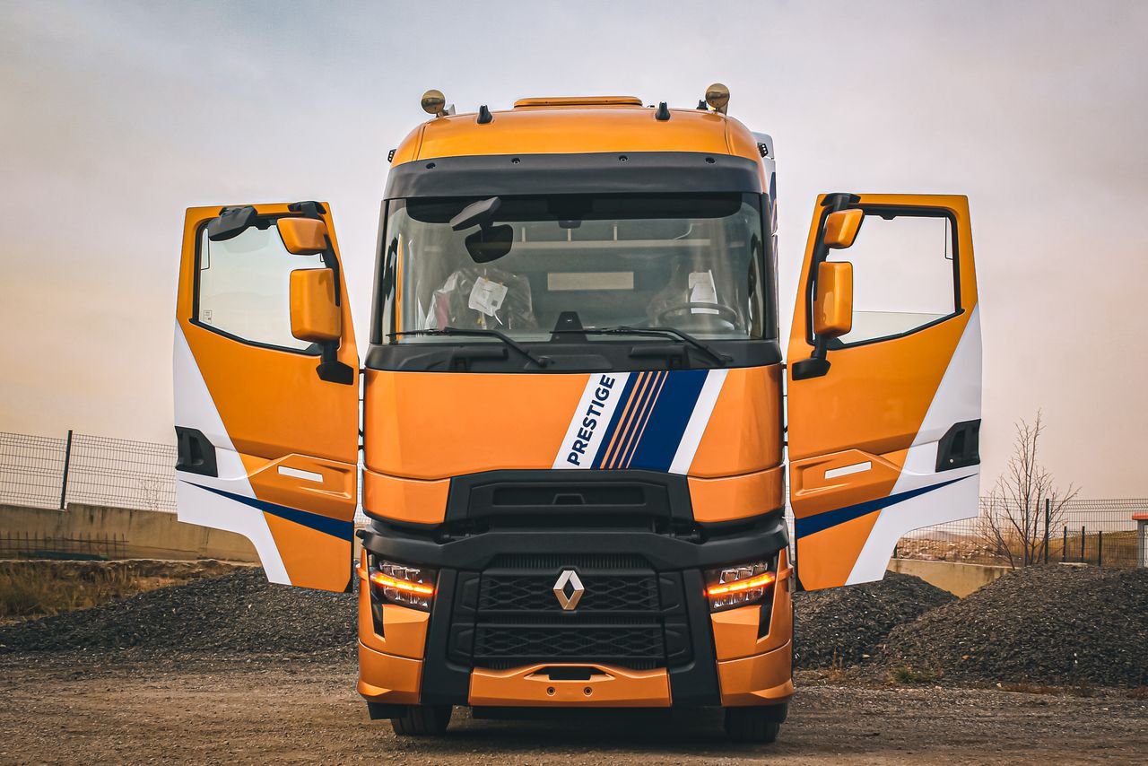 Front view of an orange Renault truck with open doors parked in a rural area.