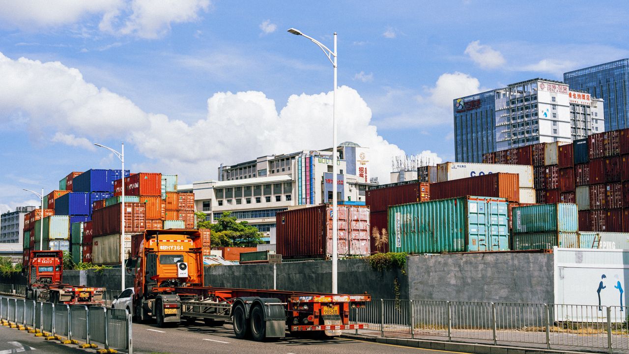 services-06 Colorful shipping containers stack at an industrial port under clear skies.